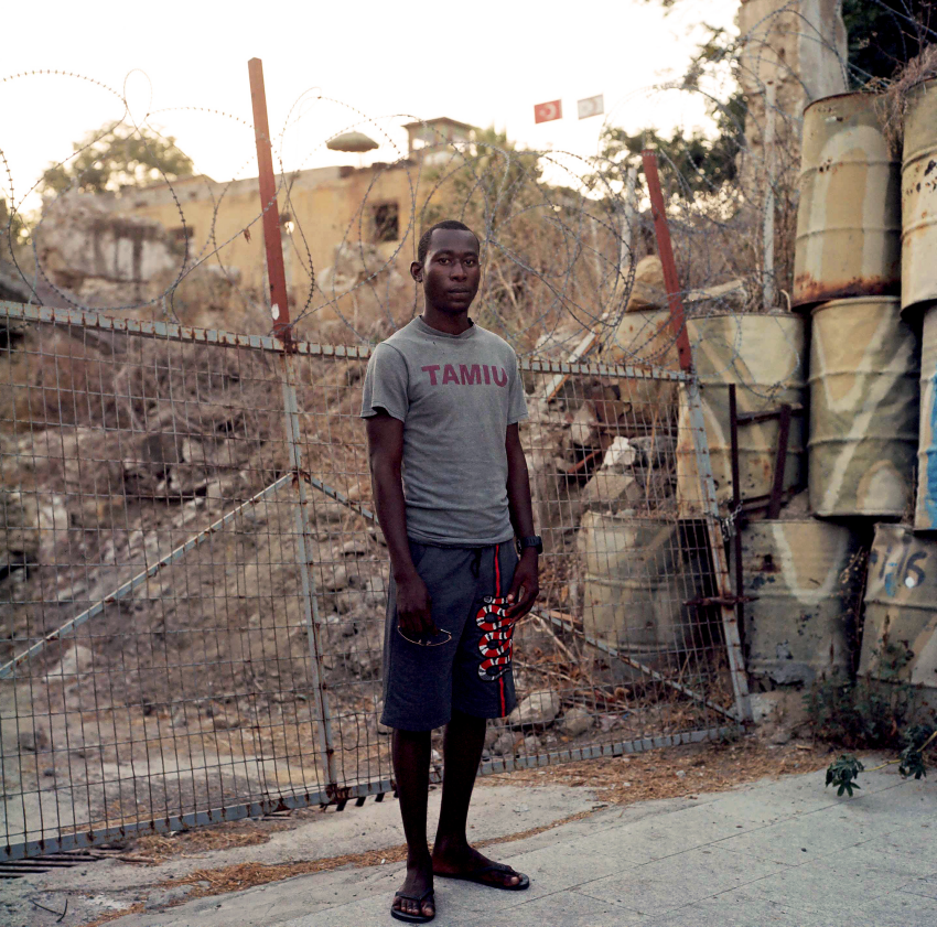 'N'. ‘N’, a migrant from Congo, poses for a portrait in front of one of the UN Buffer Zone walls separating the Republic of Cyprus and the TRNC. The city of Nicosia is the last divided city in Europe, split roughly in the middle by the UN-patrolled Buffer Zone. N left Congo in search of better opportunities and the possibility to study in Europe. Nicosia, Cyprus, August 2020. Cyprus is still reeling from the effects of the 1974 Greek-led coup and the subsequent Turkish invasion that divided the island into two communities. Yet both Greek- and Turkish-Cypriots now deal with an influx of refugees that threatens to change the island’s demographic. With a population of around 850,000, Cyprus holds the largest share of asylum-seekers per capita - 3.5 percent - in all of Europe. In the last five months of 2022, more than 10,000 asylum seekers submitted asylum claims in the Republic of Cyprus; in 2021 there were more asylum claims than births in Cyprus. These arrivals, coupled with an already broken system threaten to upend the fragile peace that has been held since 1974. As one side tries to derail the other by sending them across the border, migrants suffer while waiting in limbo, becoming the victims of racism, and extortion by landlords and employers, with no prospect of a better life. © Radu Diaconu, Canada, Shortlist, Professional competition, Documentary Projects, Sony World Photography Awards 2023