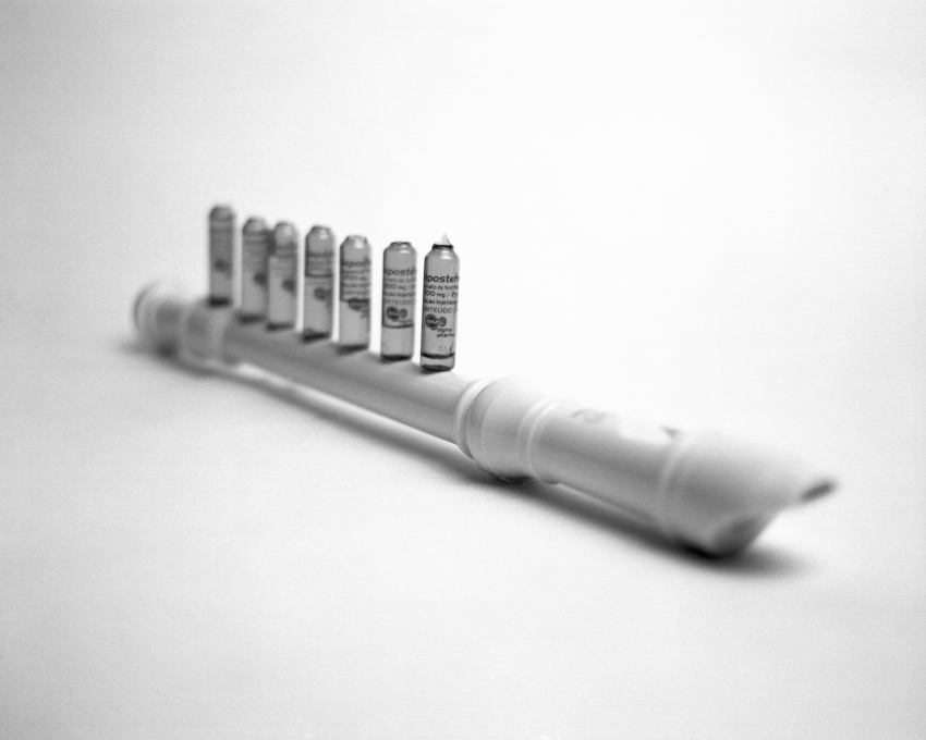 'Testosterone Notes'. Testosterone vials placed over the holes of a recorder. As notes move down the scale (a lower register), there is less liquid inside the vials. Macaia, a trans man, collects these repositories in a glass jar. The transition for him began naturally; his body has always produced more hair and his voice has always been deeper than expected. Nothing was ever wrong. A documentary series composed of photographs, films and texts about the history of voices of trans, non-binary and intersex people. The photographs are like totem poles; sculptures made for the camera that accompany biographical accounts. The starting point for this series is the story of the voice of the artist themselves, Masina Pinheiro, whose puberty transition took place at the age of 23. Their thin voice from childhood stood alongside an intuitively non-binary identity, an effeminate body with masculine expectations. The series also tells the story of voices who have undergone surgical procedures to alter decibels and conform to their gender identity. Challenging gender impositions is a determining factor that interrupts lives, especially in Brazil, the country with the highest rate of murders of LGBTQIANB+ populations in the world. © Rodrigo Masina Pinheiro, Brazil, Shortlist, Professional competition, Still Life, Sony World Photography Awards 2023 