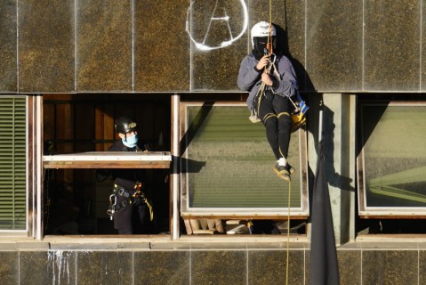 A Catalan police officer (L) talks to a squatter hanging from a building after they managed to enter the 'Kubo', one of two buildings that are to be evicted, in Barcelona, Spain, 30 November 2023. A group of squatters that locked themselves up inside two buildings resisted police efforts to enter the buildings by throwing rubble bags, smoke cans and flares to make the eviction more difficult.  EPA-EFE/Enric Fontcuberta
